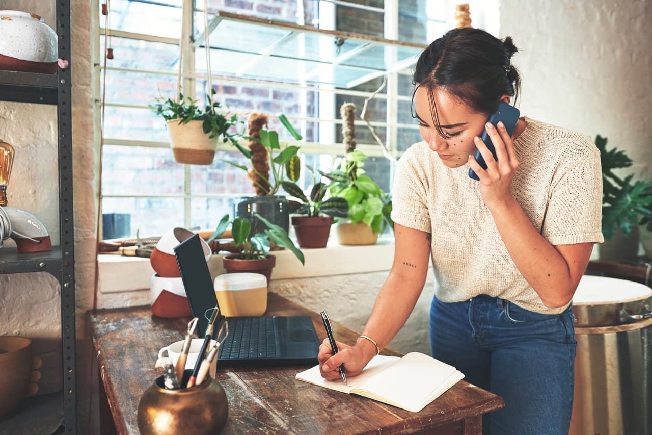 A business owner taking notes in a notebook while on a call with a customer